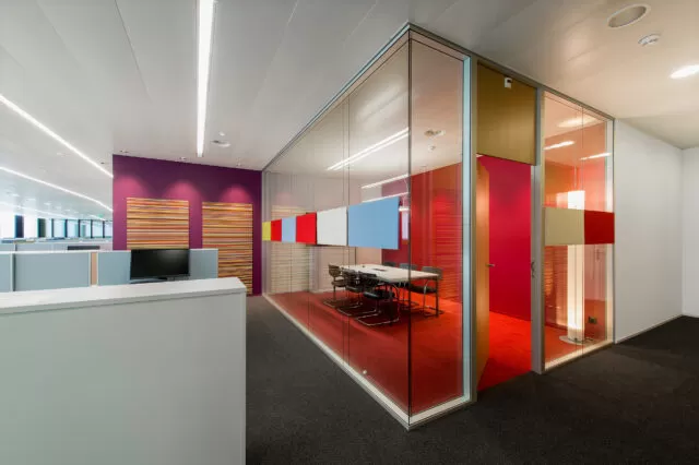 Moderner Konferenzraum mit Glastrennwänden und farbenfrohen Akustikpaneelen.